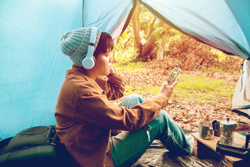 Soft focus blur Asian young man using a smartphone listening to music in the tent on holiday