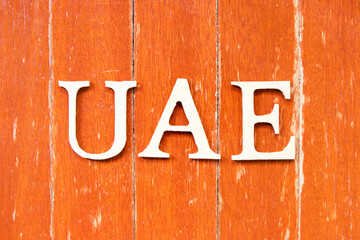 Alphabet letter in word UAE (Abbreviation of United Arab Emirates) on old red color wood plate background