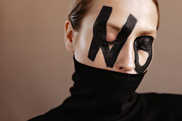 Girl with black word no on her face covered her mouth with sweater and posing with closed eyes on...