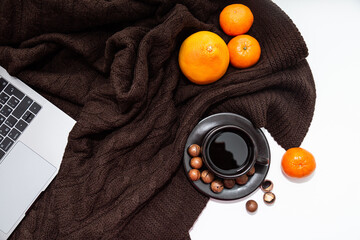Cozy home atmosphere. Laptop, cup of coffee with tangerines and nuts on a knitted brown blanket background