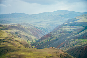 Fantasy vast landscape with vivid multicolor clay mountains. Off-road car on hill above scenic mountain valley. Colorful scenery with multi-color mountains. Off-road trip in awesome picturesque place.