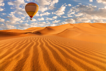 Sunset over the sand dunes in the desert with hot air balloons. Arid landscape of the Sahara desert