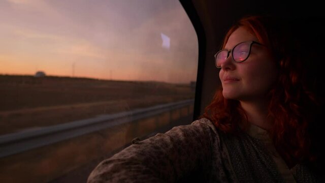 young redhead woman traveling by car at sunset, road trip, automobile travel, driving car in the countryside