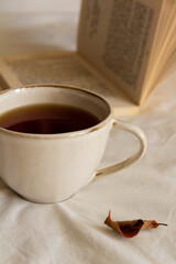 A cup of tea next to an open book on a white bed