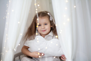 Little cute girl in a white armchair with bright Christmas lights, new year 2021 and Christmas, new...