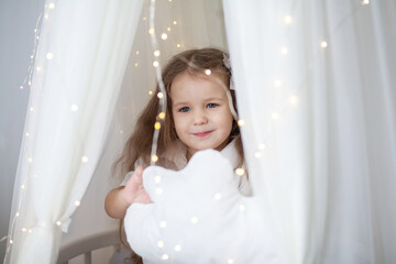 Little cute girl in a white armchair with bright Christmas lights, new year 2021 and Christmas, new...