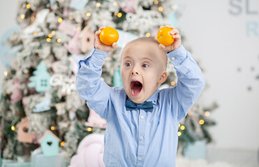 A boy with Down syndrome holds tangerines in his hands, a child sits by a Christmas tree, Christmas...