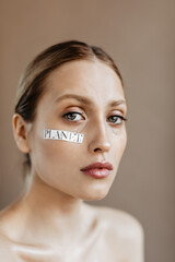 Naklejka premium Saddened woman with word planet on her cheek posing on beige background. Girl with gray eyes is crying