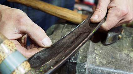 village blacksmith checks sharpness of scythe