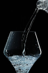 Mineral water is poured into a glass. Black background.