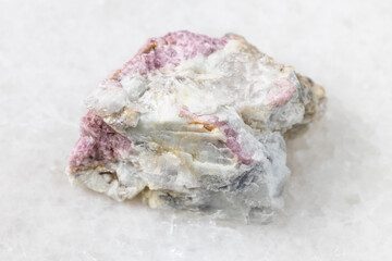 macro photography of sample of natural mineral from geological collection - unpolished pink Tourmaline mineral in feldspar and quartz rock from Kalba Range, Kazakhstan on white marble background
