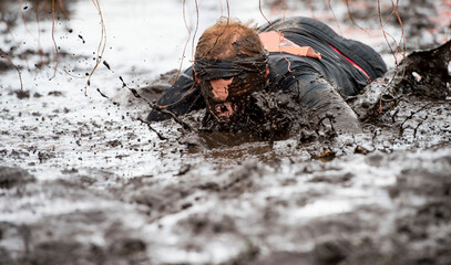 Mud race runners. Crawling,passing under a barbed wire obstacles during extreme obstacle race....