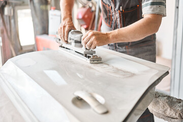 The mechanic works with a grinding tool. Sanding of car elements. Garage painting car service. Repairing car section after the accident.