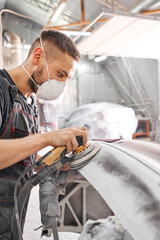 The mechanic works with a grinding tool. Sanding of car elements. Garage painting car service. Repairing car section after the accident. - 384314491