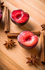Sliced red plums with cinnamon sticks and anise stars on the wooden table. Selective focus. Shallow depth of field.
