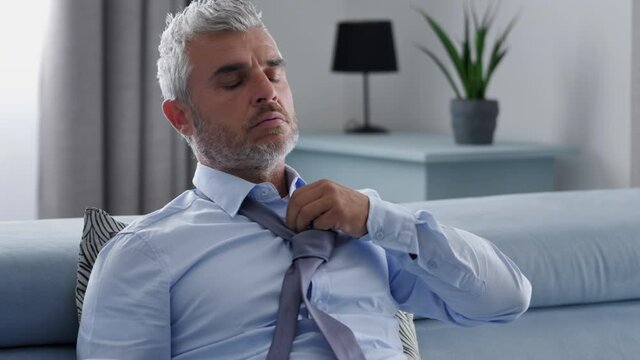 stressed overwhelmed exhausted businessman sits on the couch,tired spent man come back home after hard day work sitting on sofa unlace the tie