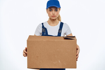 A woman in a working uniform with a box in the hands of a delivery service delivery service light background