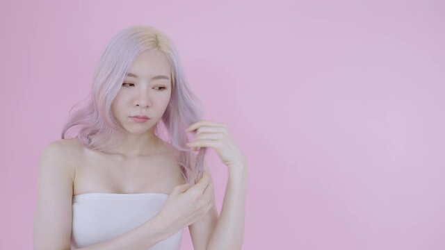Asian woman worry hair breakage with copy space for customer apply hair dye warning or tips guideline. Modern blonde and pink hair beautiful female model on isolate pink background wear sexy white bra