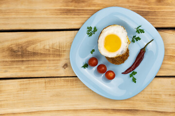 Top view of fried egg with crouton, cherry tomatoes, chili peppers on a blue plate.