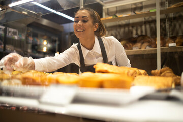Woman preparing pastry for sale in supermarket bakery department.