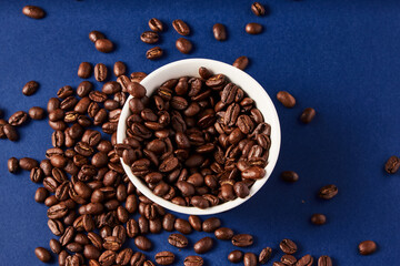 Coffee Beans in white cup spilling over to the blue background 