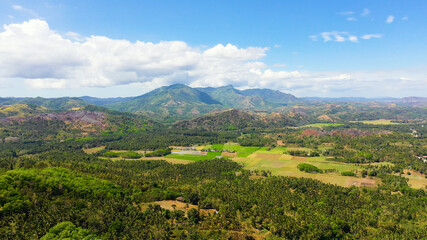 Fototapeta na wymiar Fertile farmlands with growing crops and mountains with clouds against a blue sky. Mindanao, Philippines.
