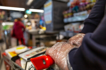 Obraz premium A man in gloves with a grocery cart in the supermarket. Close-up. Coronavirus pandemic.