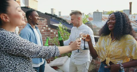 Attractive positive multiethnic friends having fun together on balcony,drinking beer and wine and smiling lots during summer party,close up