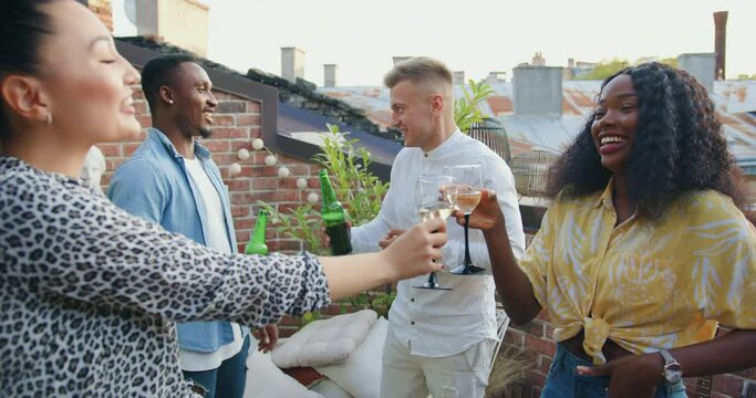 Attractive positive multiethnic friends having fun together on balcony,drinking beer and wine and smiling lots during summer party,close up
