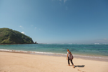 Back view of a woman with a backpack on the ocean on nature, walk on empty sand beach, leaving footprints