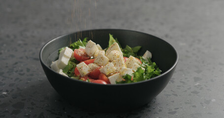 ground spices to salad with mozzarella, cherry tomatoes and frisee leaves in black bowl on terrazzo surface