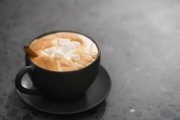 cappuccino with marshmallow and cinnamon in black cup on terrazzo surface with copy space