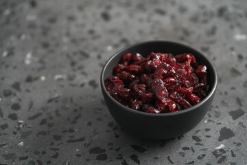 Dried cranberries in black bowl on concrete surface