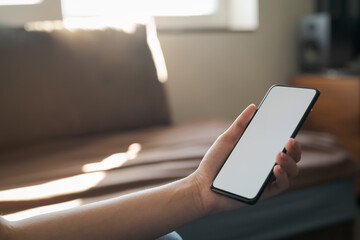 Young woman hold smartphone with white screen while sitting on a couch