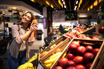 Positive brunette woman holding coconut at grocery store fruit department. Buying fruit at supermarket.