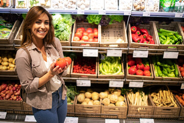 Woman standing by the shelf full of vegetables and holding tomatoes. Healthy food promotion.