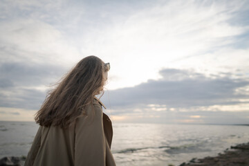Obraz premium pretty girl walking on a beach in beige trench coat with warm evening light