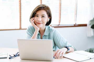 Happy young beautiful Asian Freelancer woman using laptop  computer and wireless earbuds working...