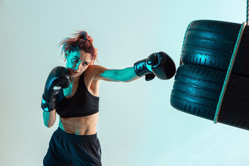 A female fighter in Boxing gloves strikes the tires with her hand