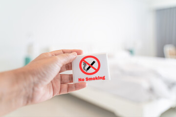 human's hand holding no smoking sign with blurred bedroom , in soft focus