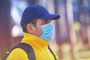 A man traveler in a medical face mask (respirator) outdoors. The man walks in the forest