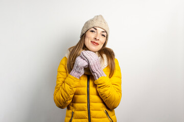 Young woman in a warm hat and mittens is smiling on a light background. Winter concept, winter fashion, winter clothes. Funny mood, emotions, surprise, shock