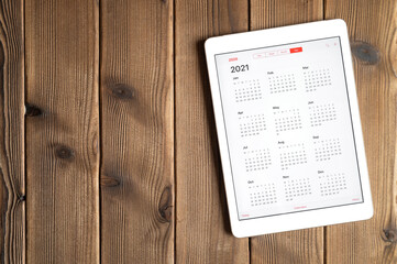a tablet with an open calendar for 2021 year on a wooden boards table background. space for text