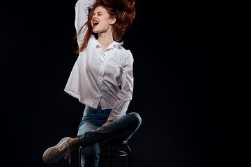 pretty woman sitting on a chair posing white shirt jeans long hair red lips dark background