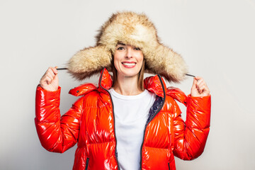happy young girl in a red jacket and a fur hat on a light background. Concept fashion, shopping,...