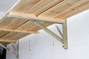 Close-up of a wooden shelf supported by a triangular iron frame on the wall