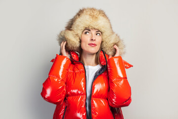 young girl in a red jacket and a fur hat, looks up on a light background. Fashion concept, trend