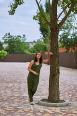 a girl in a green suit stands on the street near a large tree