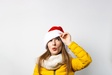 Young woman looks out from under Santa Claus hats wearing eyes on a light background. Concept of winter, winter holidays, Christmas, New Year. Funny mood, emotions, surprise, shock
