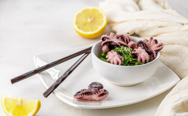 Croped photo of green wakame seaweed salad with sesame seeds and mini octopus served with chopstick at the restaurant